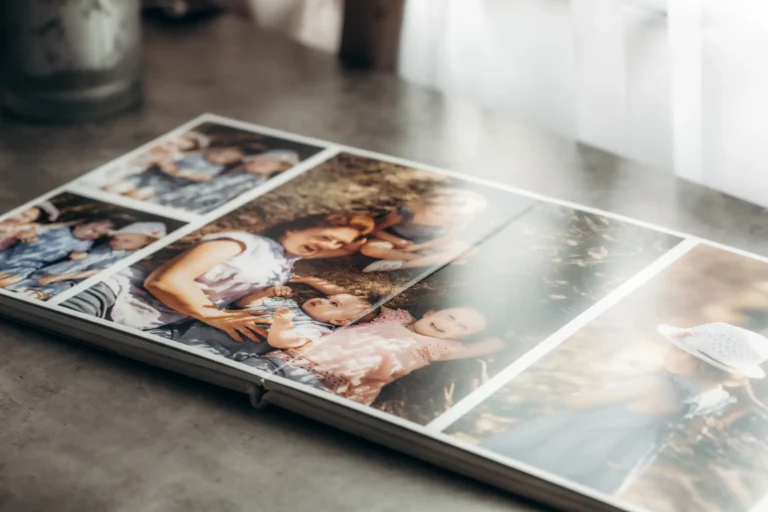 An open photo album lies on a table, displaying several photos of a woman with a young child in different outdoor settings. The images capture warm moments, even harking back to a newborn photoshoot. Some show the child in a hat, with sunlight filtering through, casting a gentle glow over the pages.